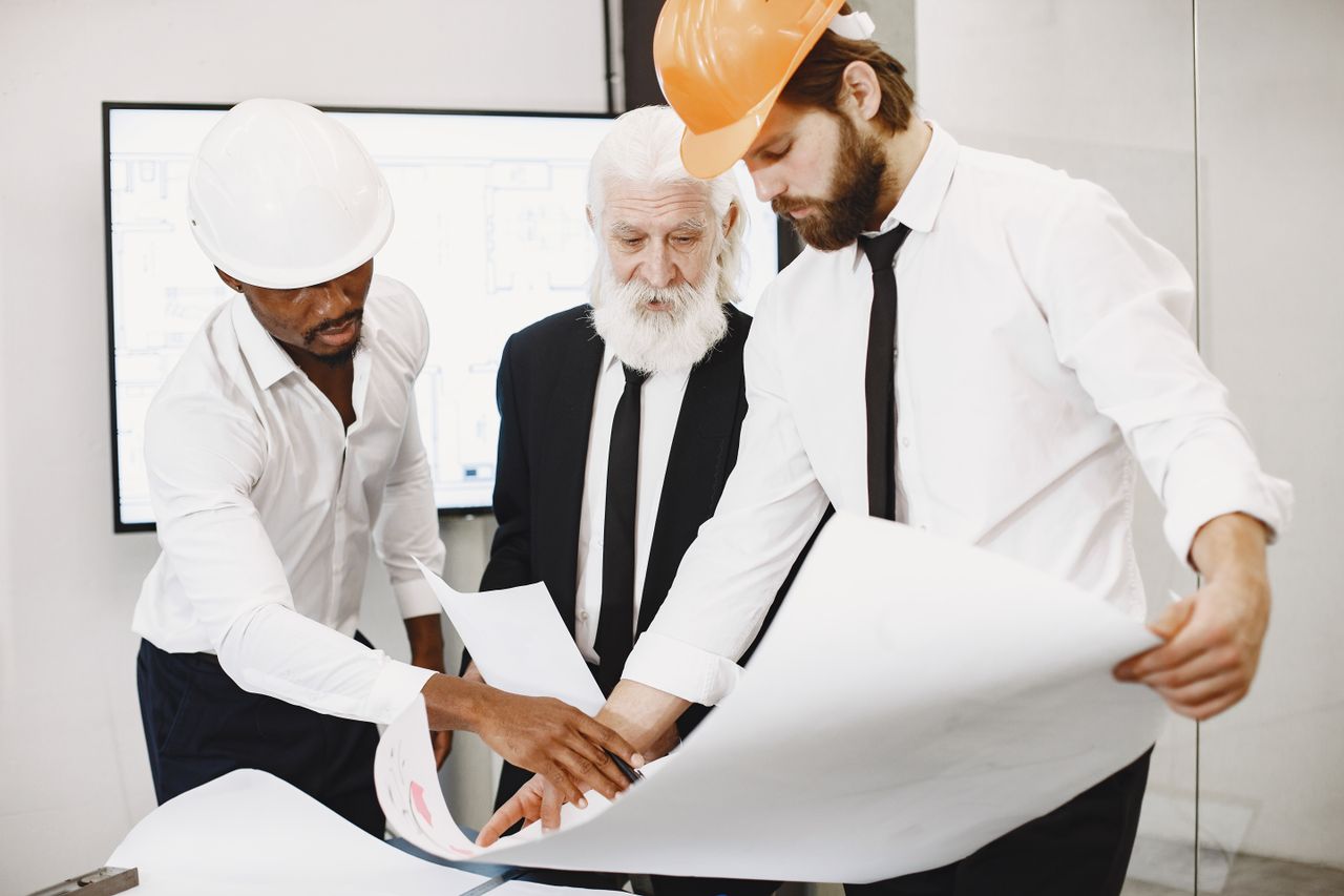 services-01 Three architects in office reviewing blueprints, showcasing teamwork and professional attire.